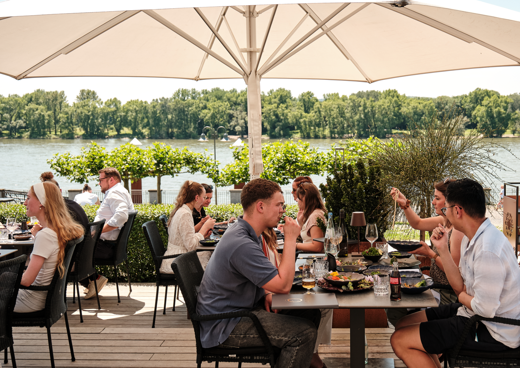 Eine Gruppe Gäste genießen ihre Getränke und ihr Essen auf der Terrasse mit Rheinblick